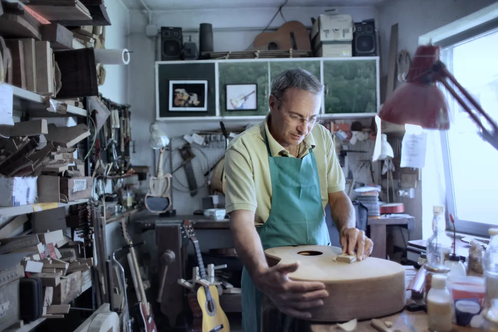 A luthier working alone on a guitar body at his workshop bench