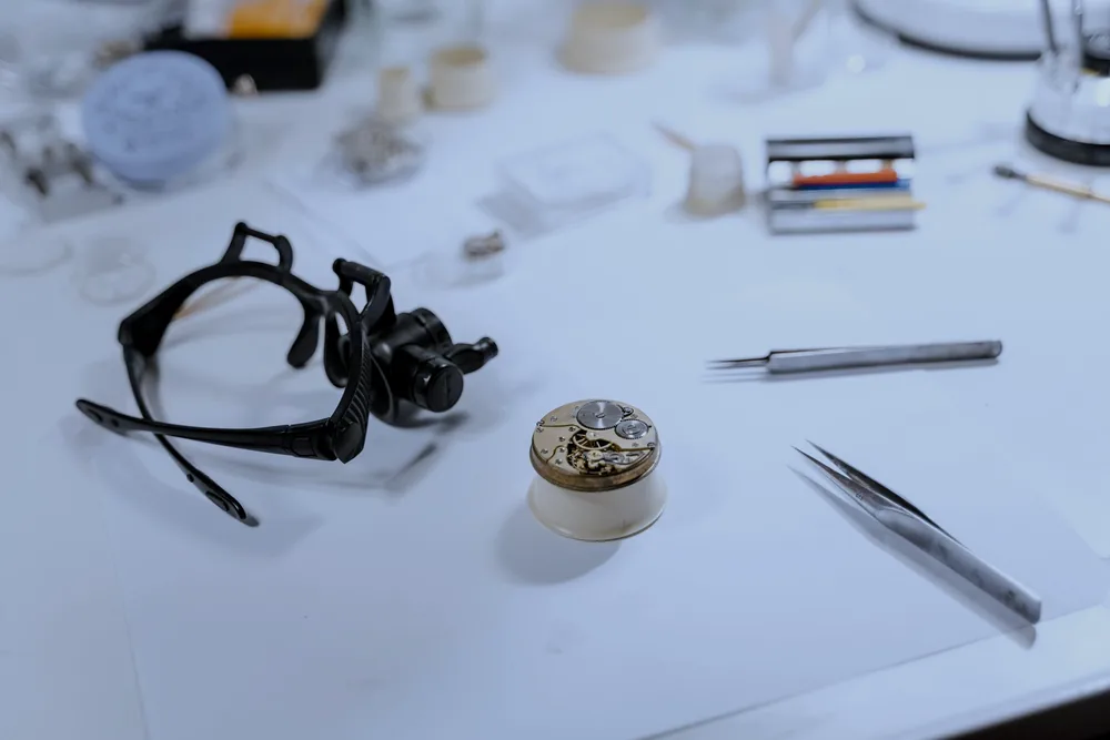 A watchmaker's bench with a loupe, tweezers and a watch movement part way through a repair